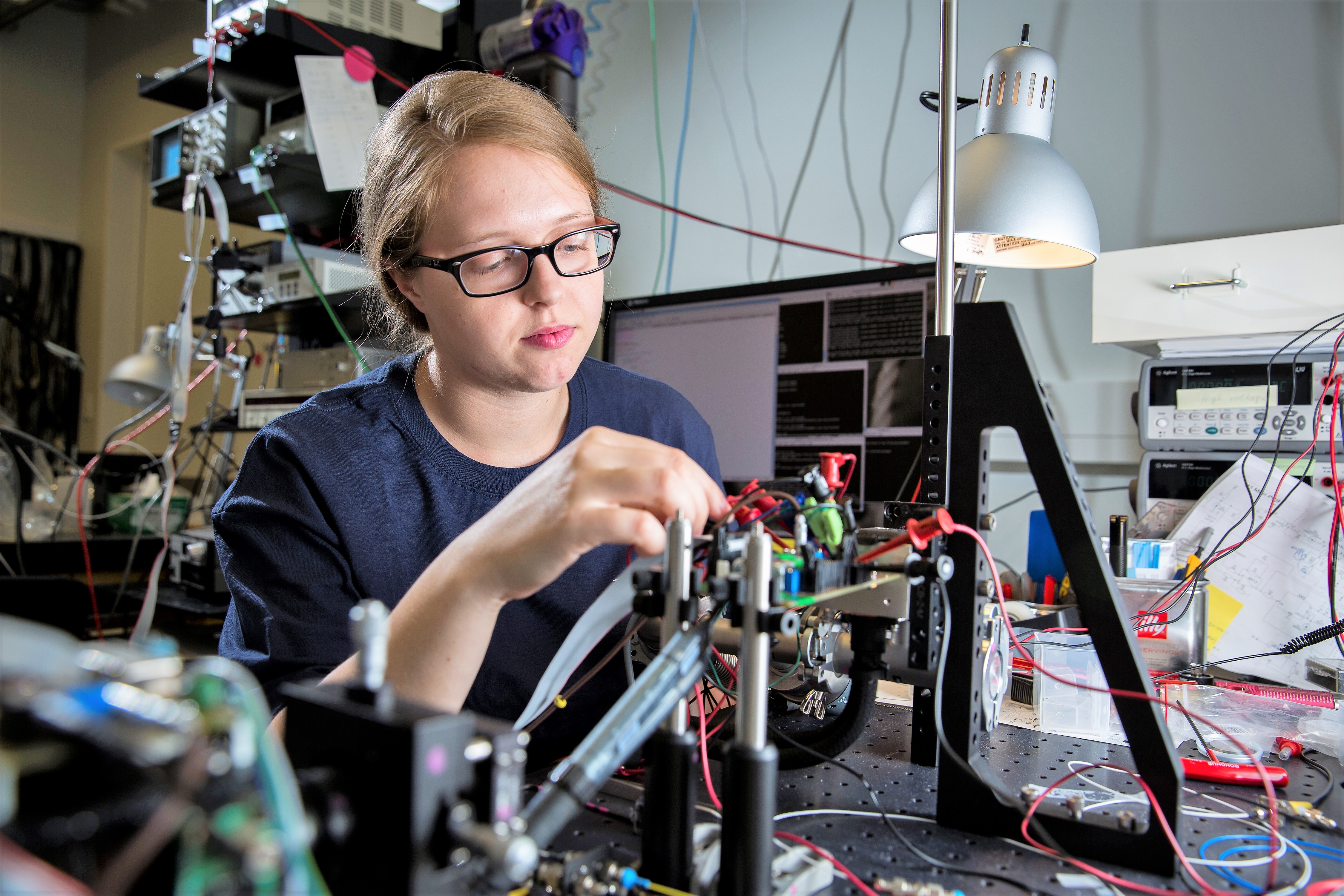 Sarah in a dark lab with optical fibers glowing red and green wrapped around her